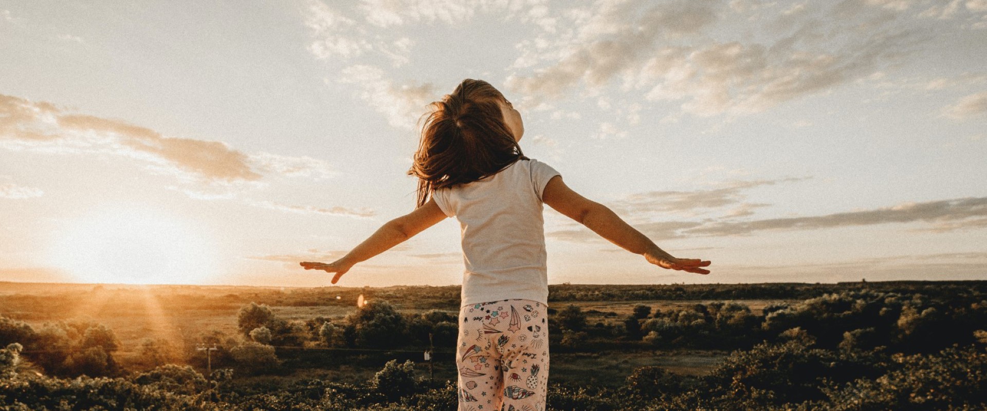 Cover picture of the article: Children's Day Activities - Algarve. In the photo, a child looks up to the sky with open arms while standing on a dune.